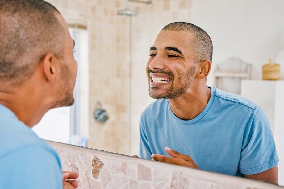 man looking at teeth in the mirror